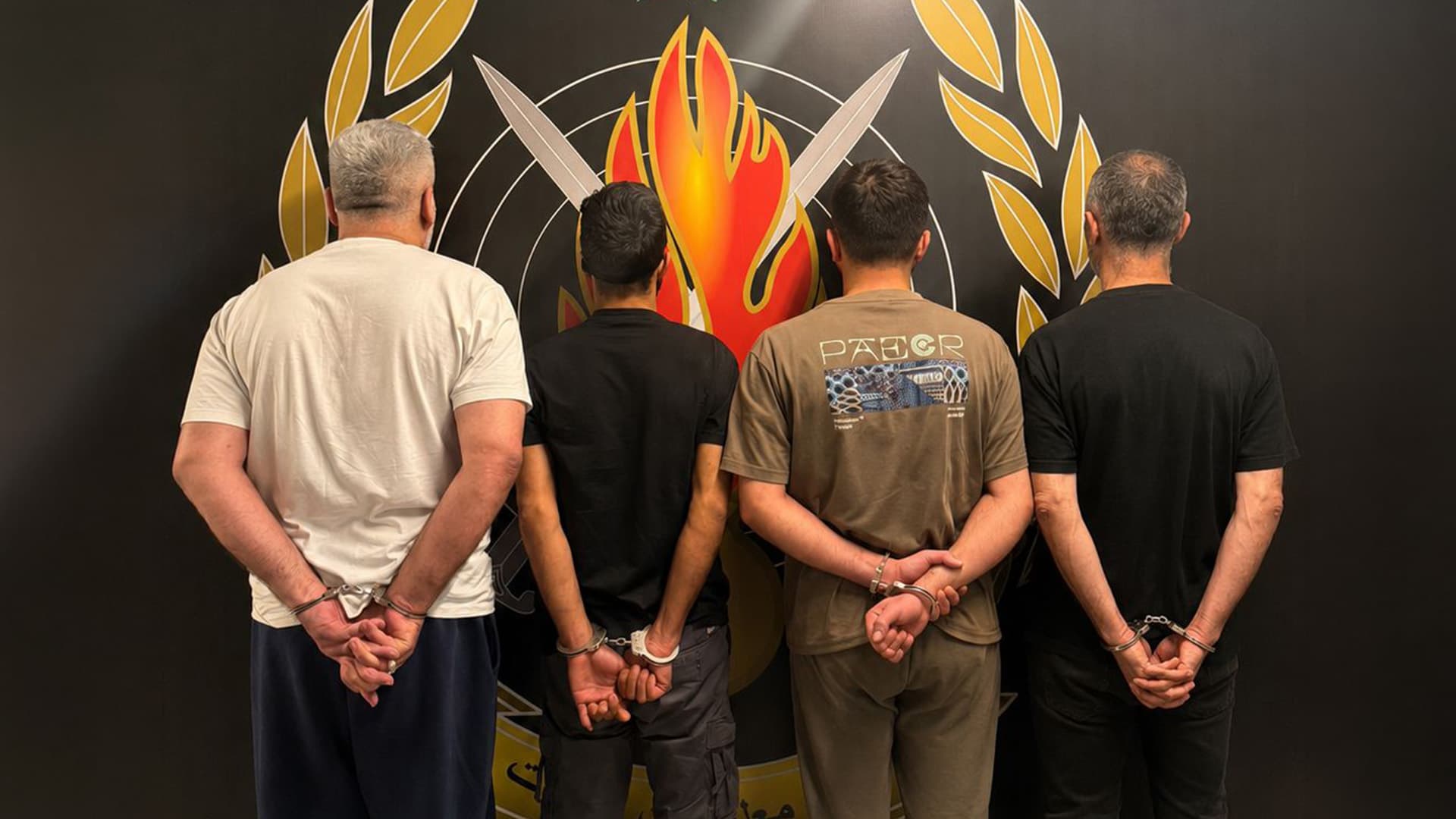 Four detainees photographed from behind in front of the Information Branch emblem